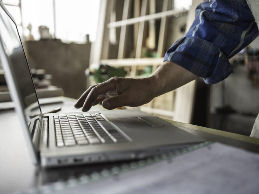 Bouwer typt op laptop in zijn werkplaats en volgt tips voor foutloos calculeren van de klus
